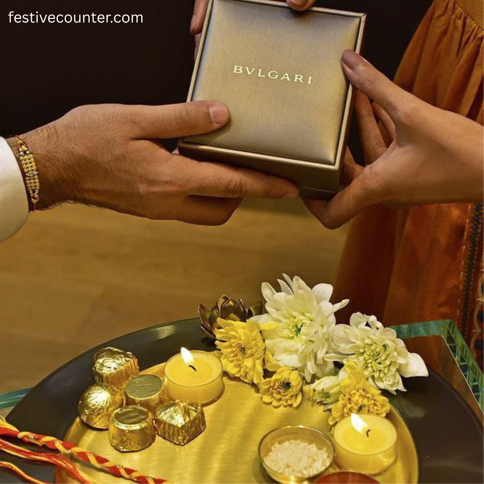 Raksha Bandhan Gift Exchange with Luxury BVLGARI Box Hands exchanging a BVLGARI gift box during Raksha Bandhan, with a gold tray decorated with flowers, candles, chocolates, and a Rakhi.