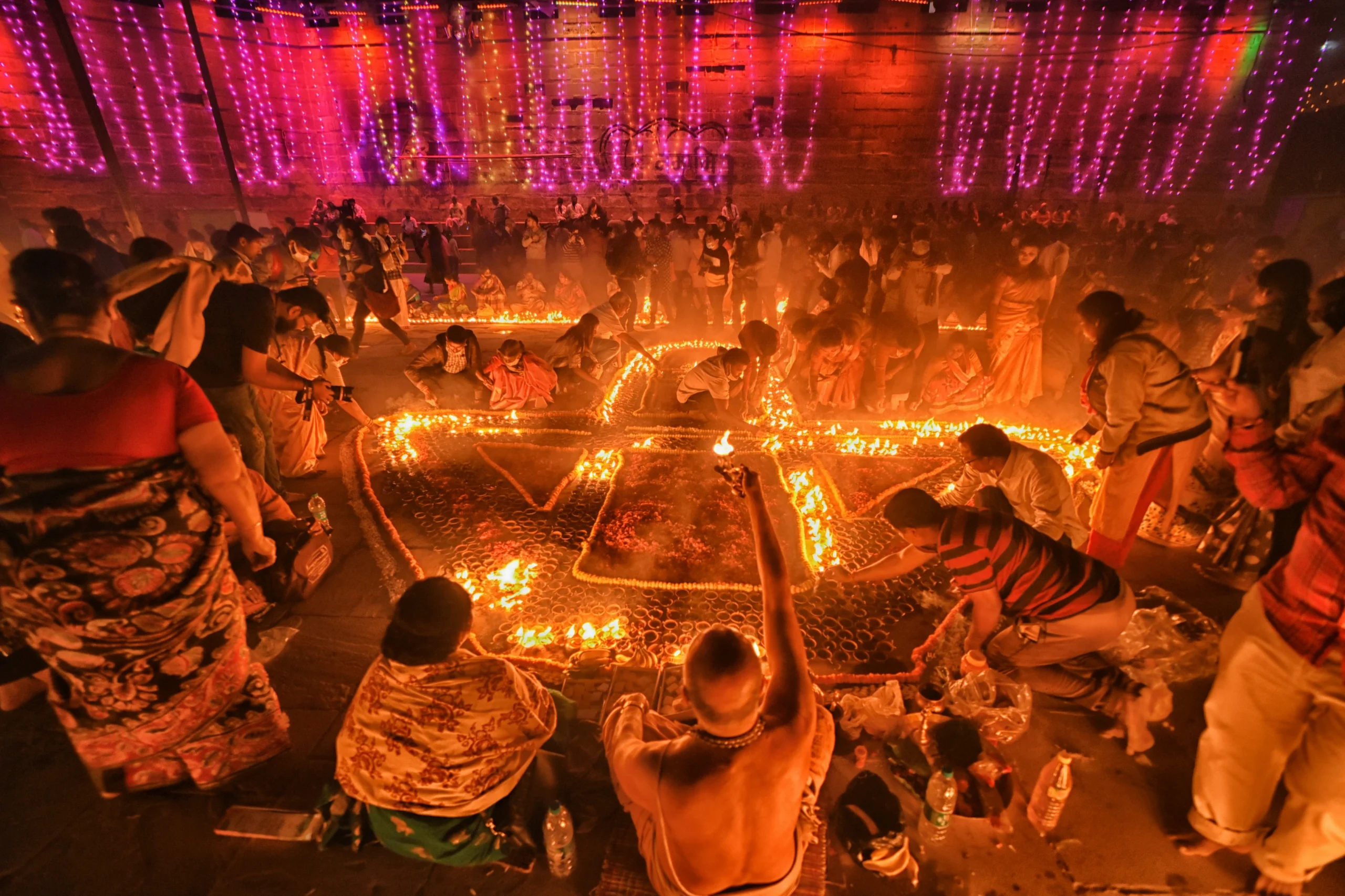 DIwali Poja People gather around intricate fire patterns on the ground during a cultural or religious ceremony, with colorful lights hanging in the background, celebrating the Diwali Countdown and honoring Sikhism religion traditions.