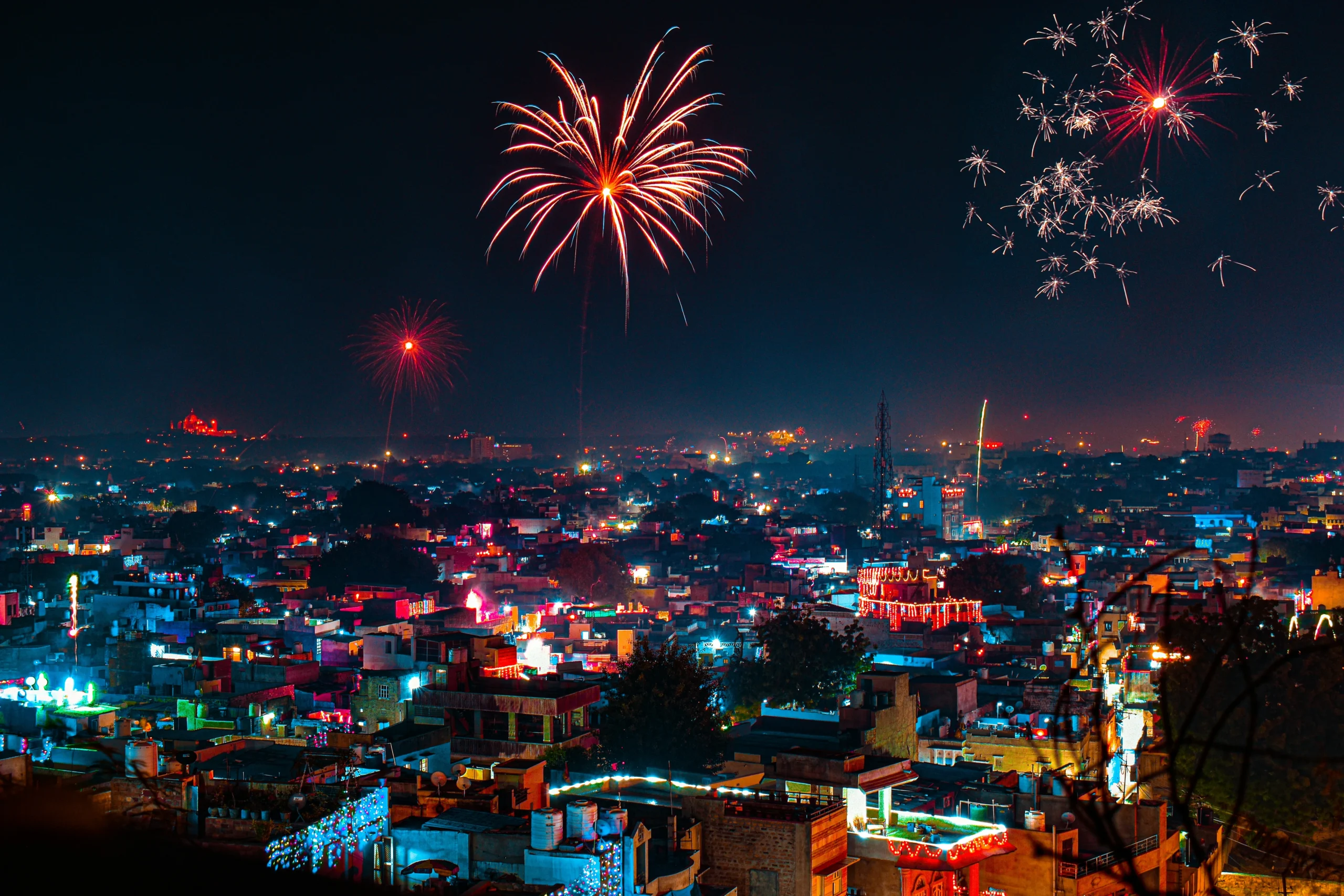 Diwali Firecrackers A vibrant cityscape at night with colorful fireworks lighting up the sky. Illuminated buildings below create a festive, lively atmosphere.