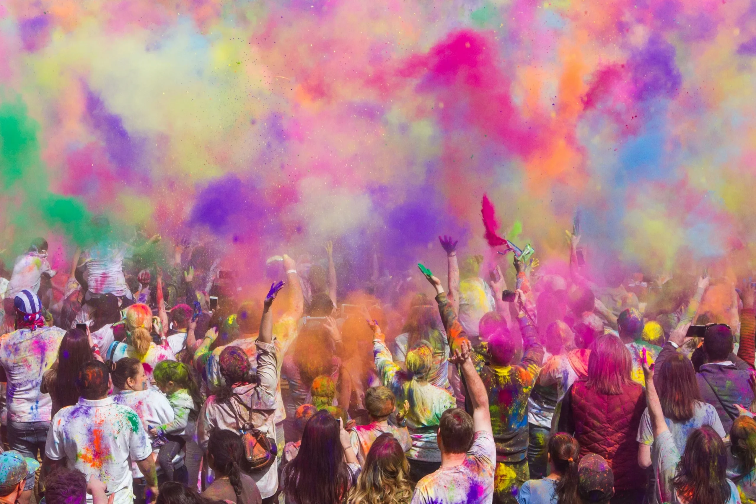 holi people A crowd of people throws colorful powder into the air during an outdoor Holi festival, filling the scene with vibrant clouds of color.