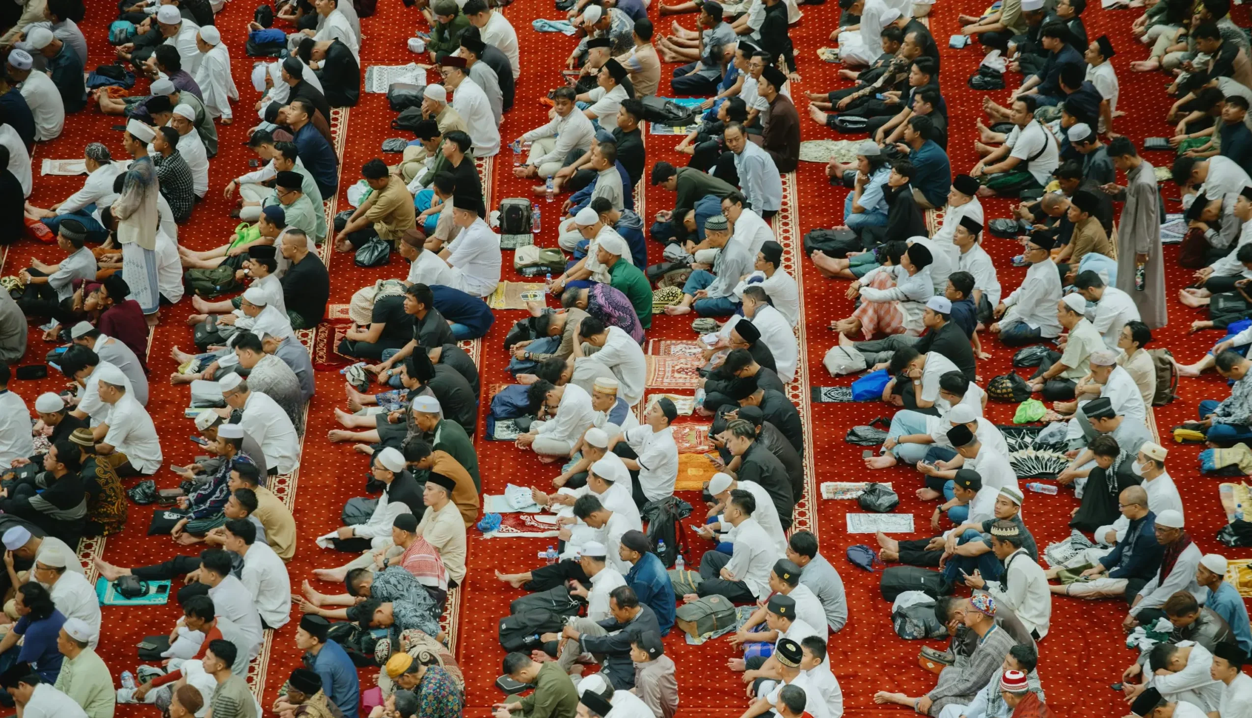 A large crowd seated on the floor of a mosque, celebrating Eid al-Fitr together in a communal gathering.