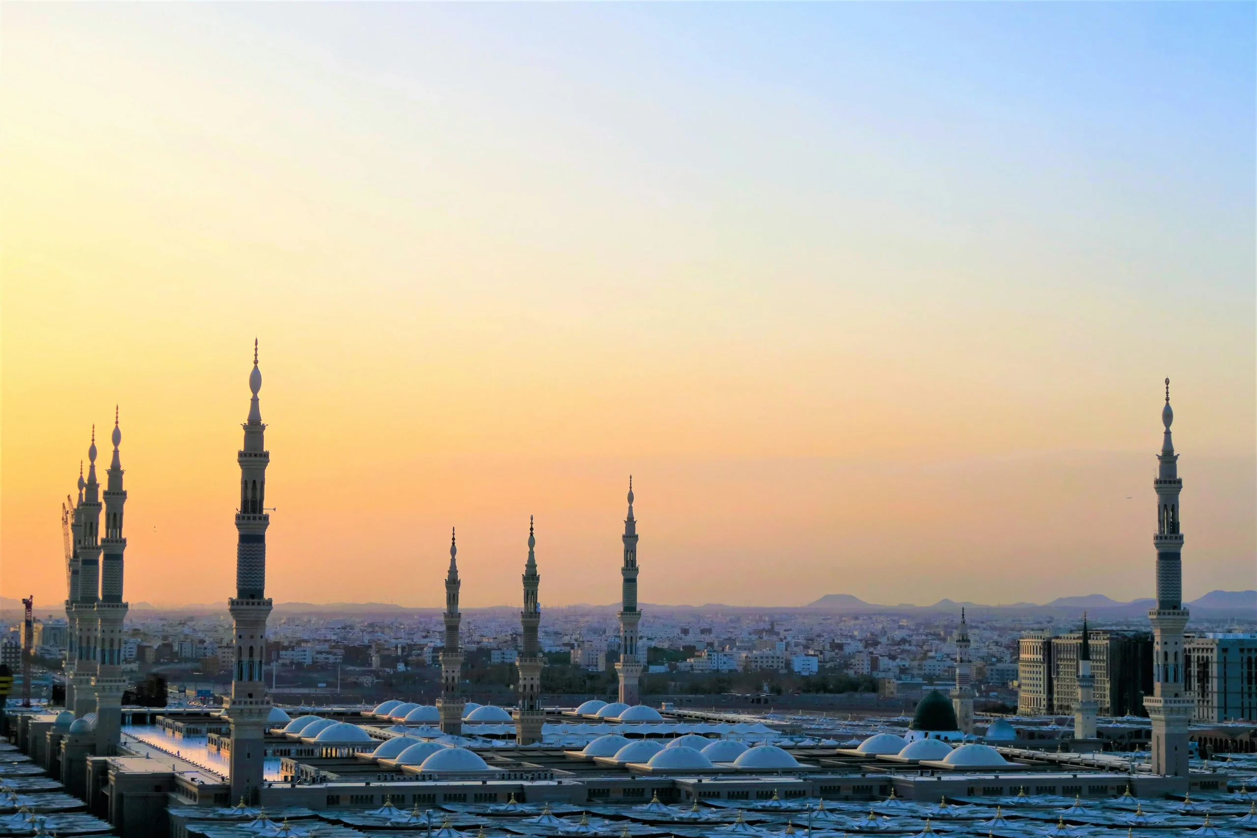 Sunset view of a cityscape with tall, ornate minarets silhouetted against an orange sky. The scene conveys a serene and peaceful ambiance.