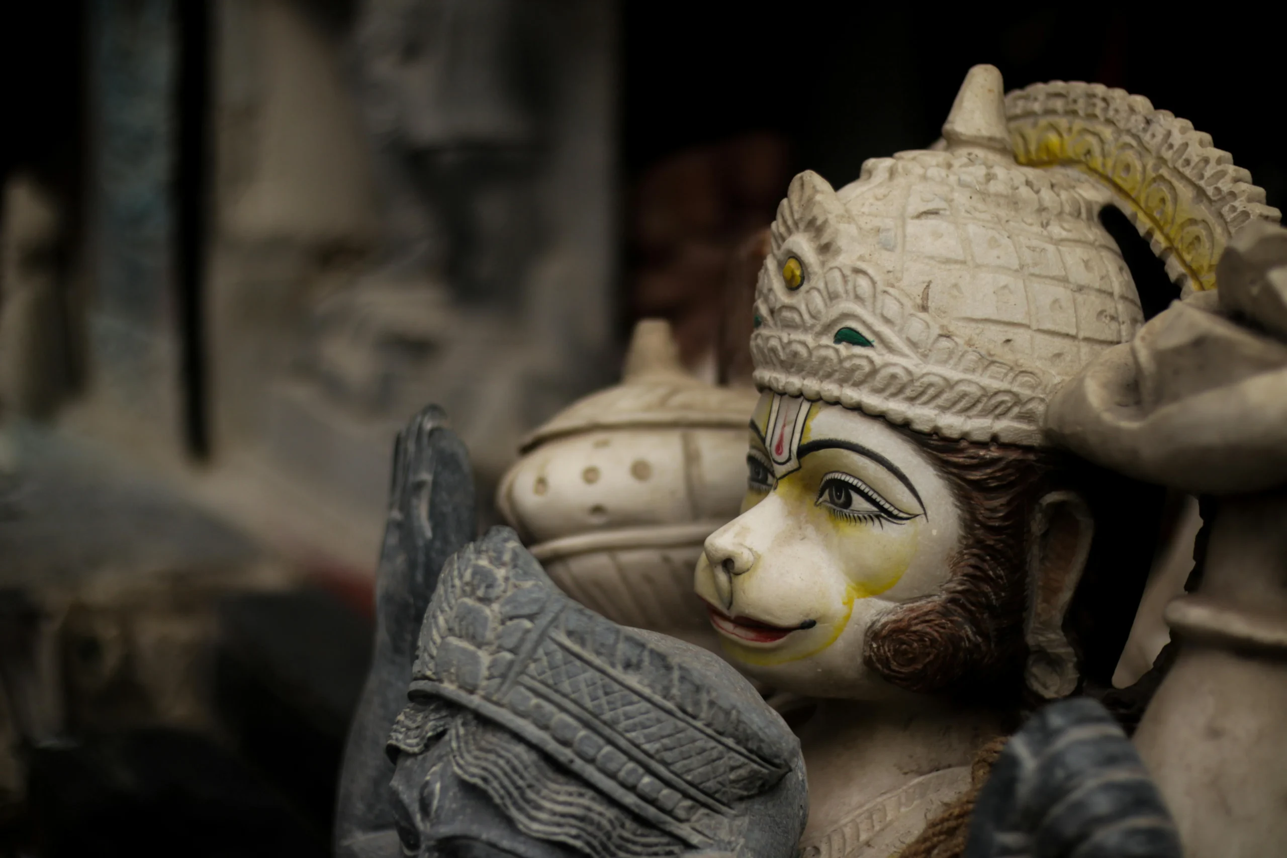 Close-up of a detailed Hanuman statue with a serene expression and ornate headpiece, captured against a blurred background, evoking spirituality.