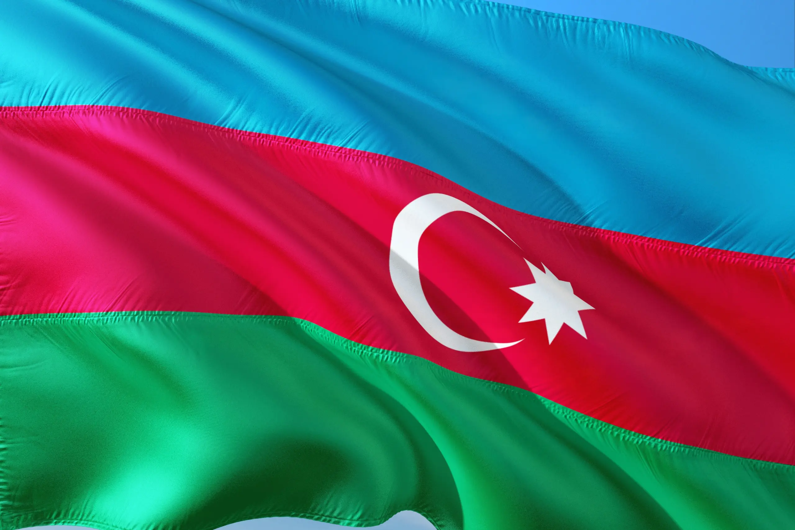 Flag of Azerbaijan waving in the wind with blue, red, and green stripes and a white crescent and star.