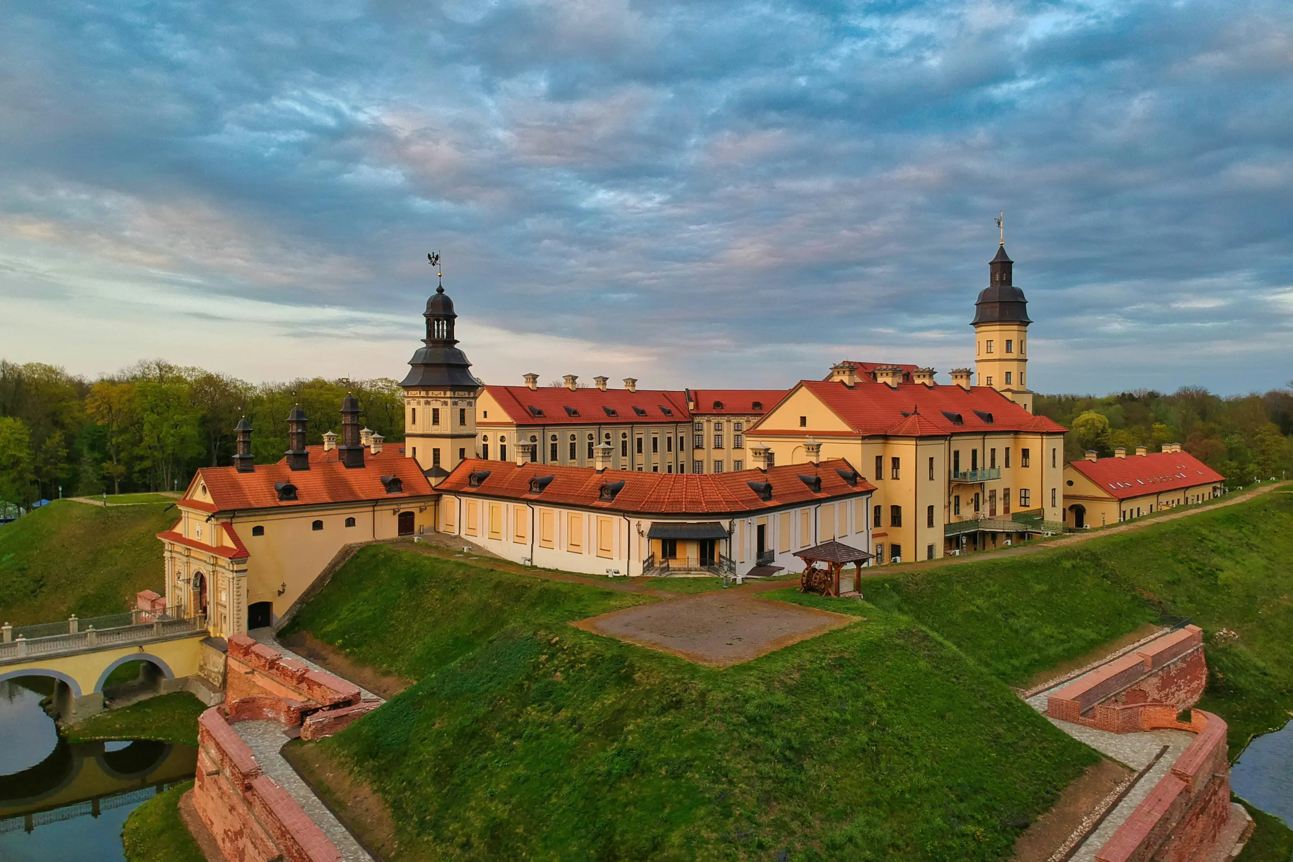 Scenic countryside view in Belarus with green fields, forests, and a soft sunset glow.