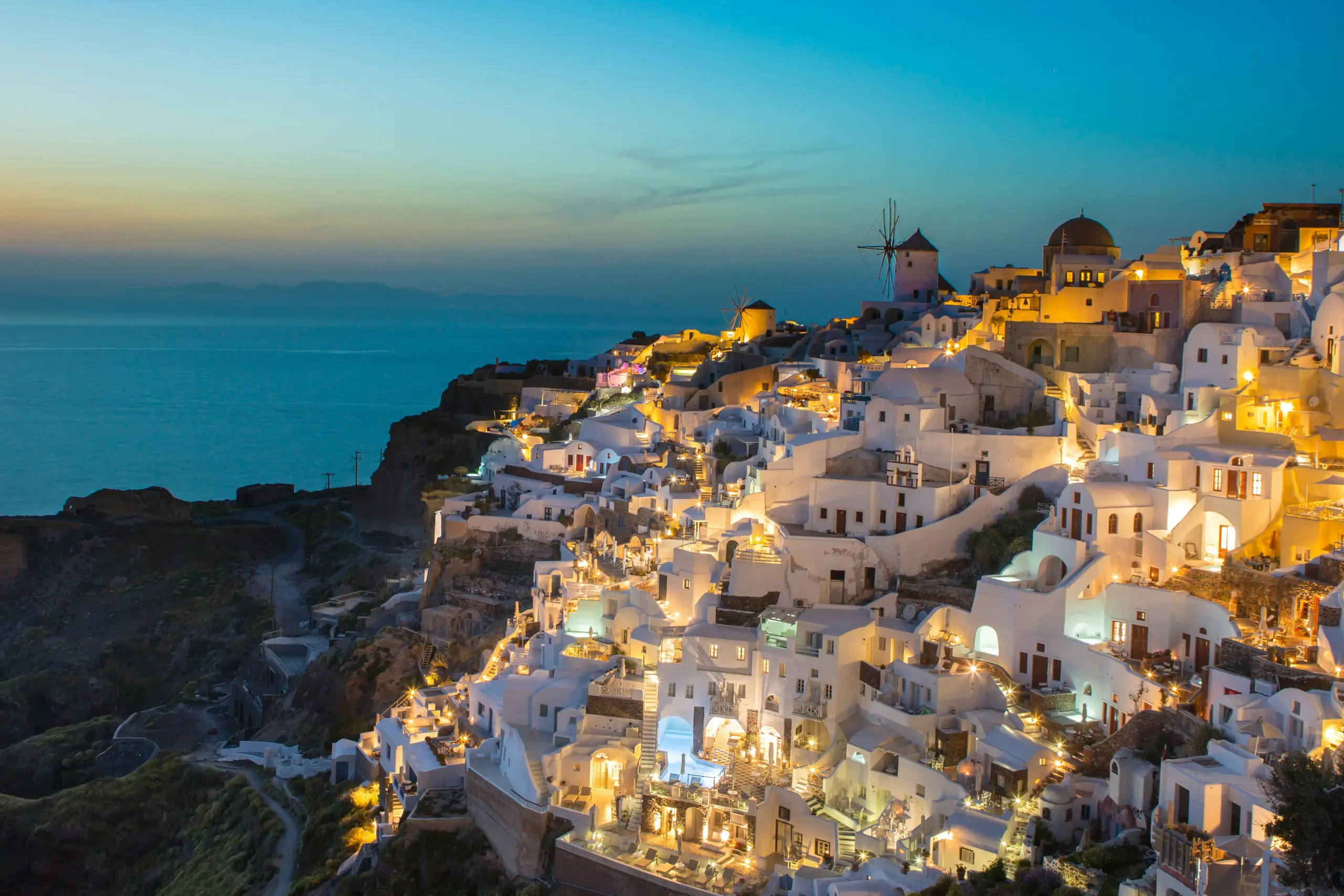 Night view of a Greek city with glowing lights, illuminated buildings, and a scenic skyline.